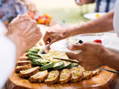 Close-up of unrecognizable people putting food on their plates. Family celebration outside in the backyard. Big garden party.